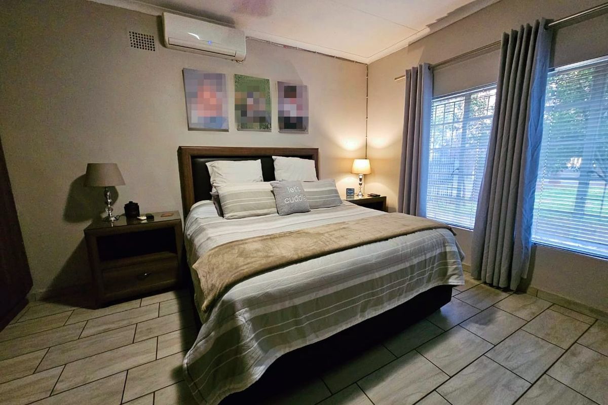 A well-maintained bedroom featuring tiled flooring, a wall-mounted air conditioning unit, and large windows with fitted curtains.