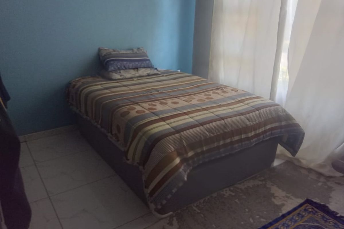 A bedroom featuring tiled flooring and a blue accent wall, with natural light provided by a window covered by curtains.