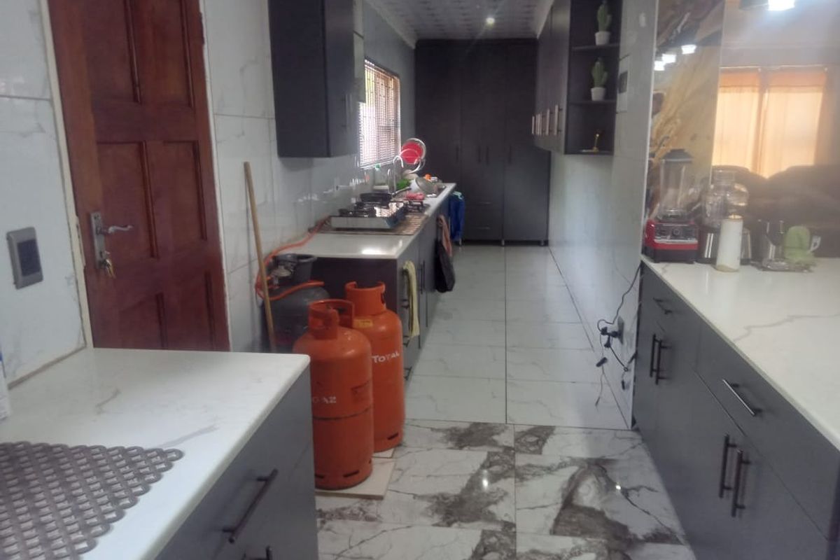 A galley-style kitchen featuring dark cabinetry, marble-look floor tiles, and integrated gas cooking facilities.