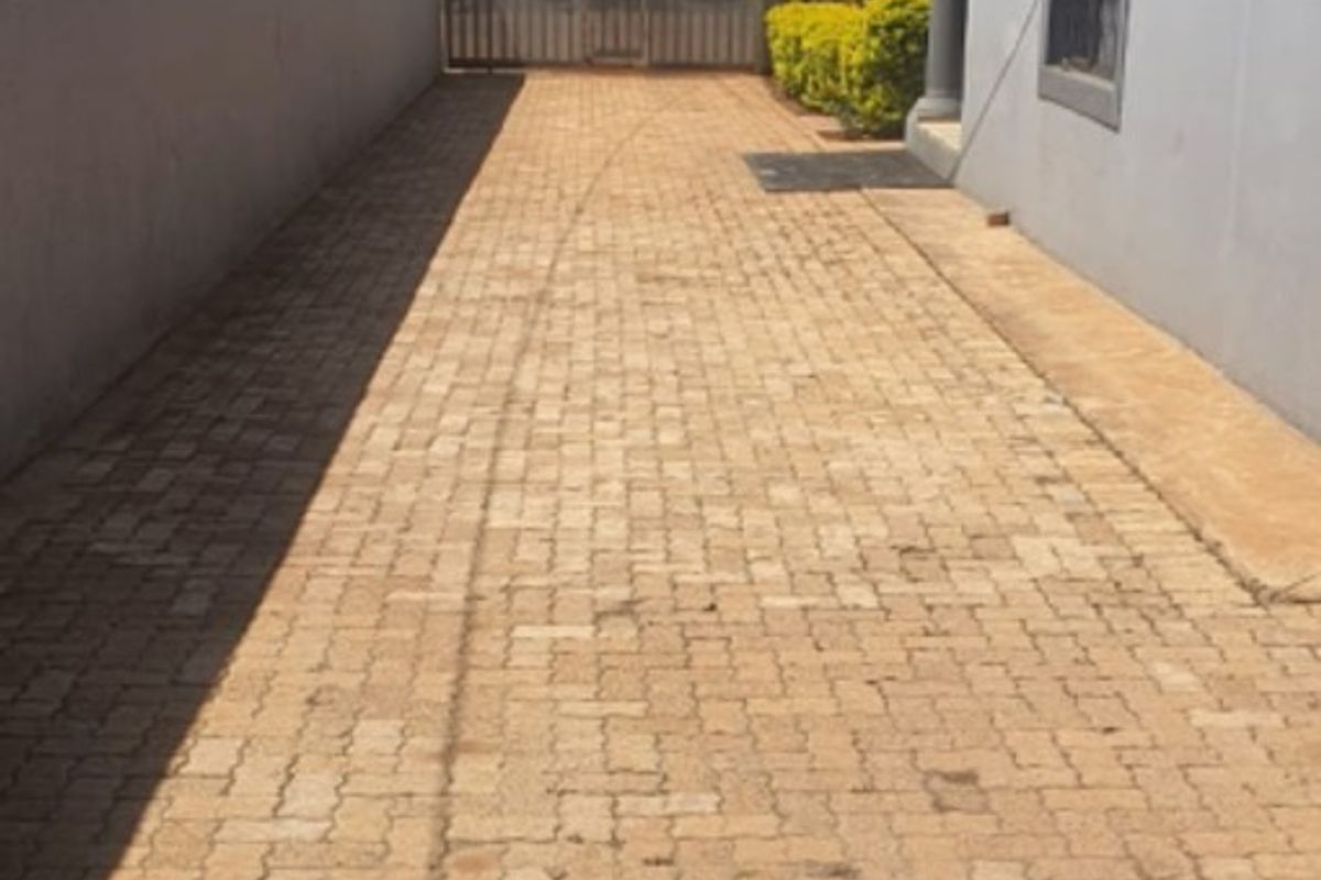 A paved side driveway or walkway area leading to a rear gate, featuring perimeter walling and exterior building access.