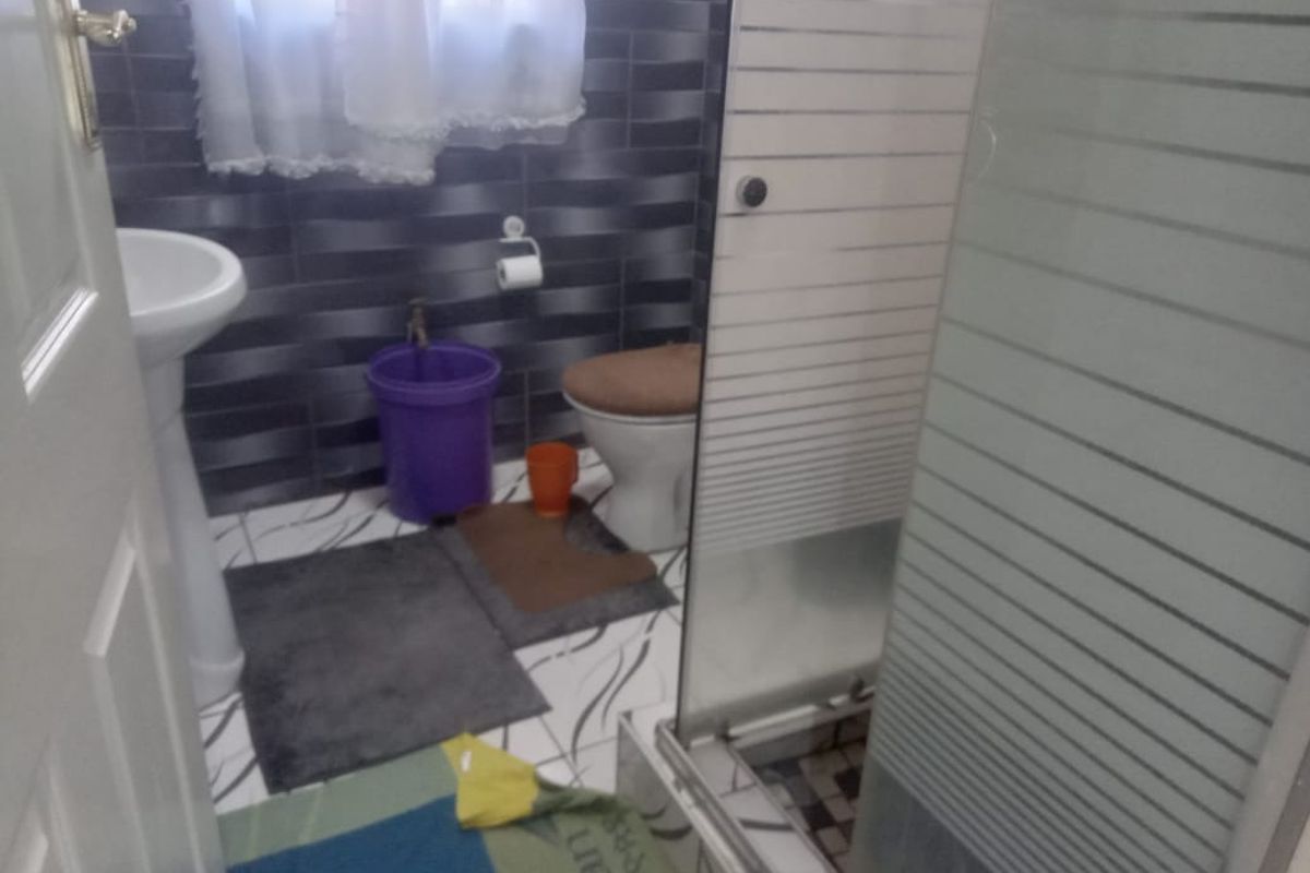 A compact bathroom featuring a pedestal sink, a standard toilet, and a glass-enclosed shower stall with horizontal frosted detailing.