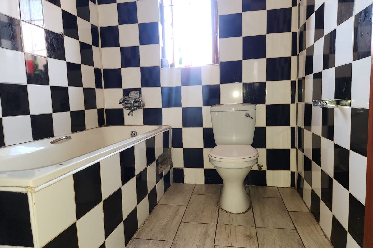 A dated bathroom featuring a bathtub and toilet with high-contrast black and white checkered wall tiles and wood-look floor tiles.