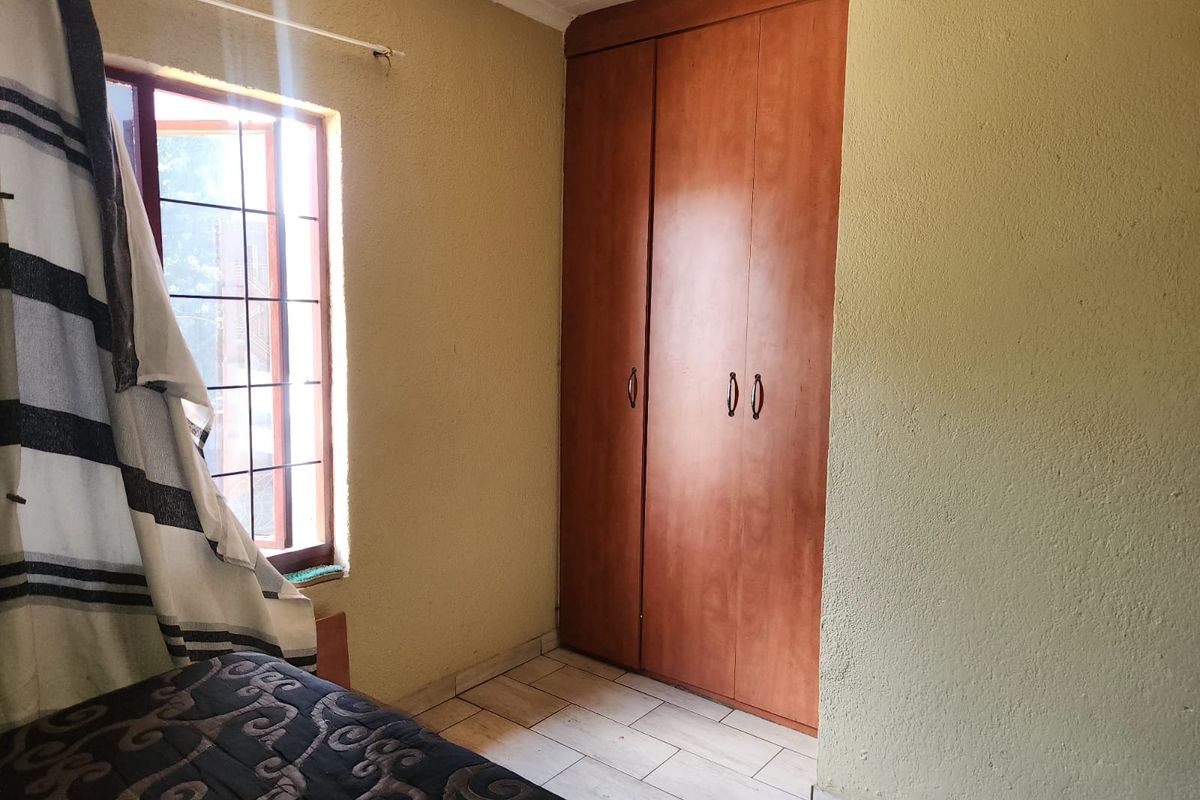 A bedroom featuring built-in wooden cupboards and tiled flooring, providing functional storage space.