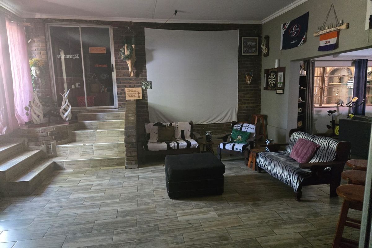 Spacious living area featuring tiled flooring, exposed brick feature wall, and tiered steps leading to a glass sliding door entrance.