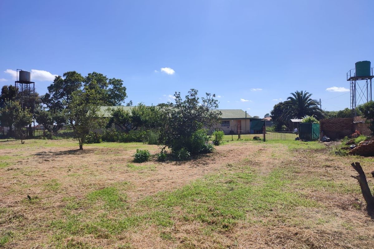 A spacious residential plot featuring established trees, two elevated water tanks, and a view of the existing dwelling structure.