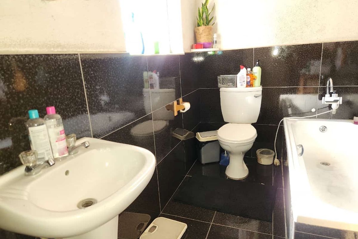 A functional bathroom featuring a pedestal basin, a standard toilet, and a bathtub with dark wall and floor tiling.
