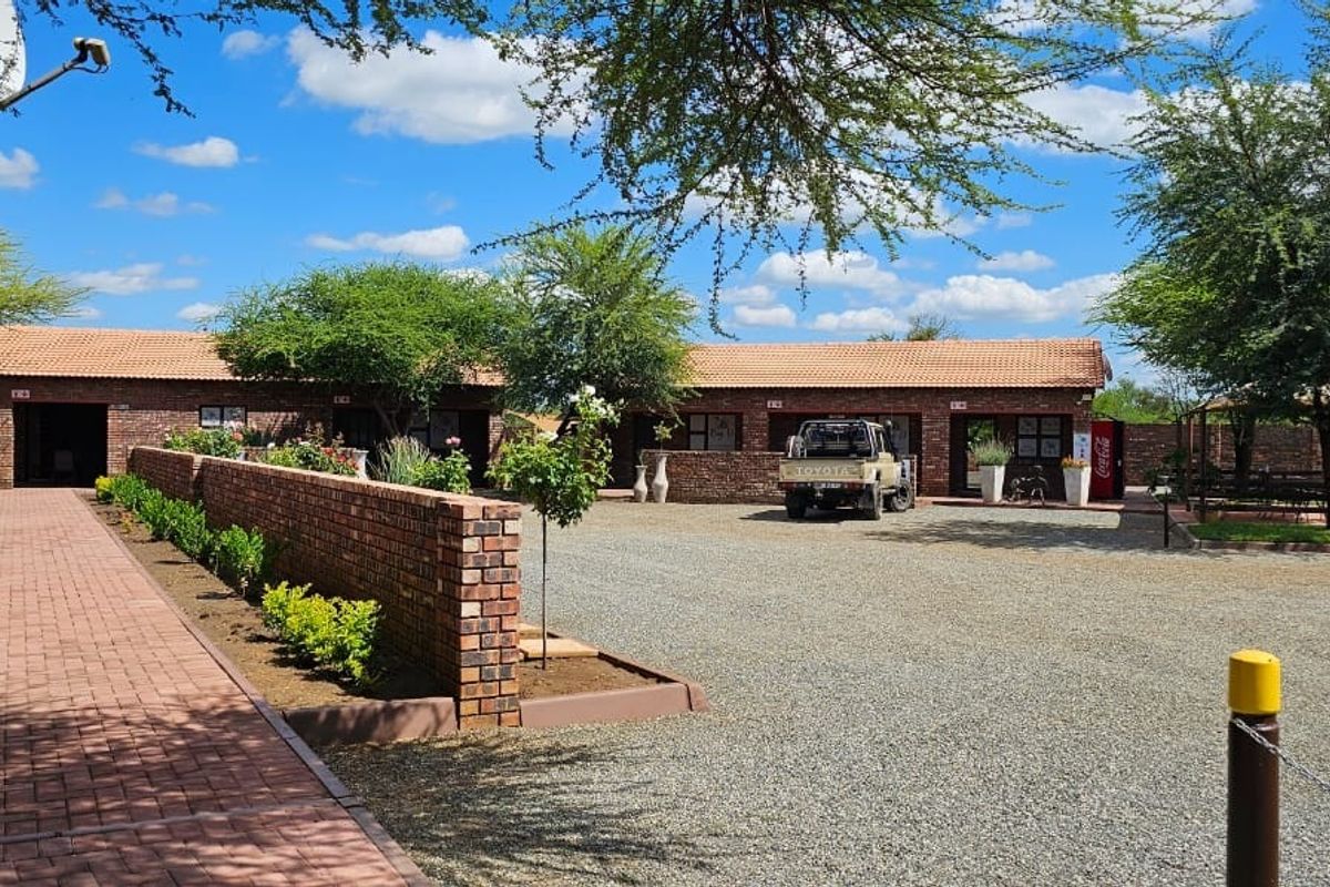 A spacious farm courtyard featuring brick-paved walkways, face-brick building exteriors, gravel driveway, and established landscaping under a clear blue sky.
