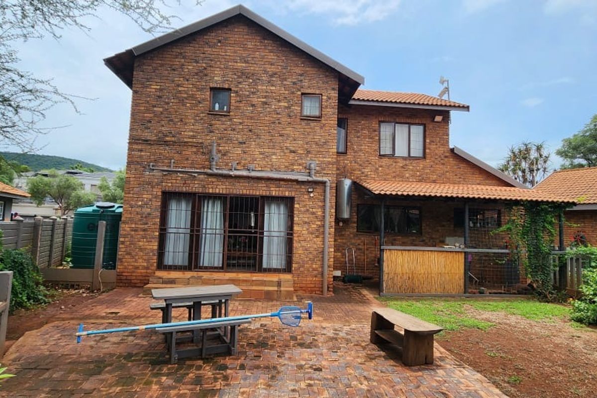 Rear view of a double-story brick house featuring a paved patio area, built-in braai, and a small garden space.