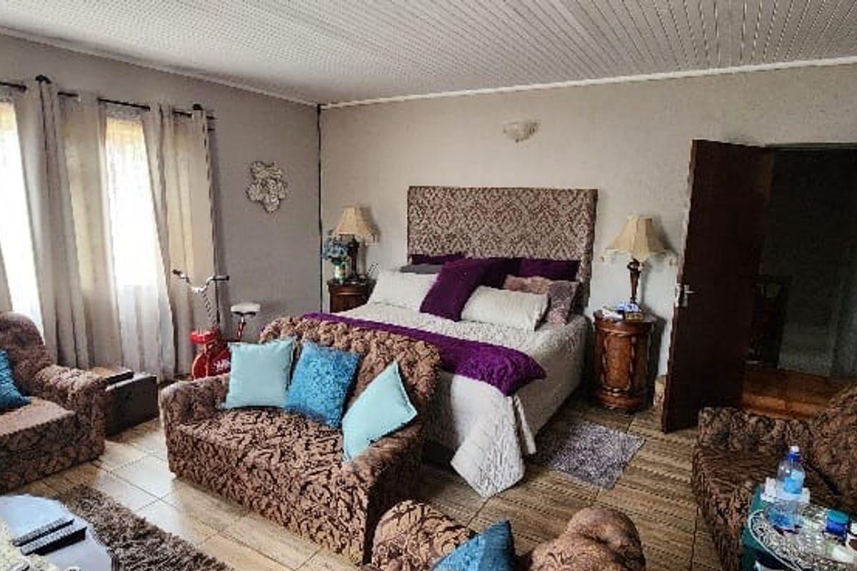 A spacious bedroom featuring tiled flooring and a timber panelled ceiling, offering a comfortable layout with direct access to an adjoining room.