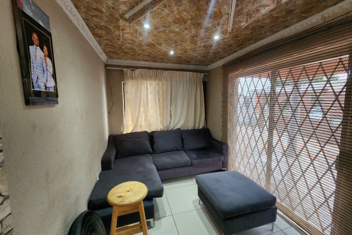 A living room featuring tiled floors, recessed lighting, and a decorative ceiling, with access to an outdoor area through a sliding glass door.