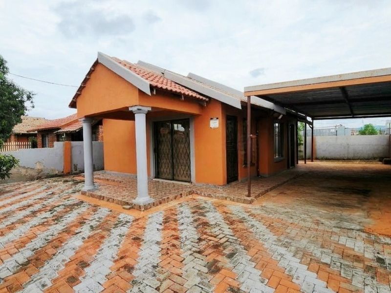 Front view of a single-story house featuring a tiled roof, covered carport, and paved driveway with a secure entrance.
