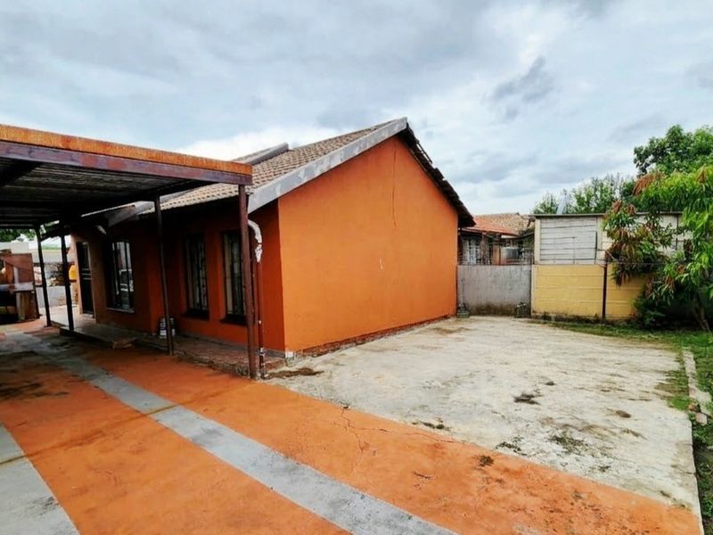 Rear exterior view of the property featuring a concrete driveway, a metal carport structure, and a tiled roof with visible signs of wear.