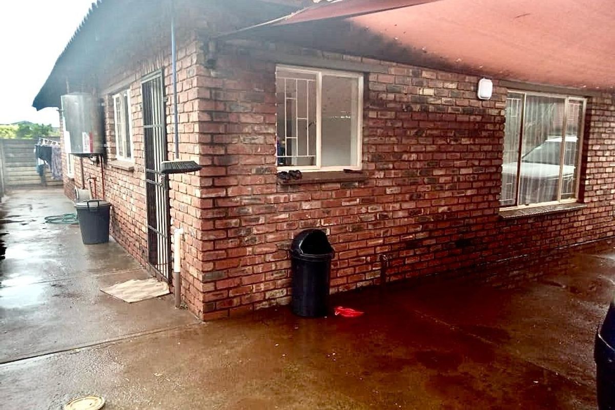Exterior view of the rear brick facade featuring a covered patio area, security bars on windows, and an external geyser unit.