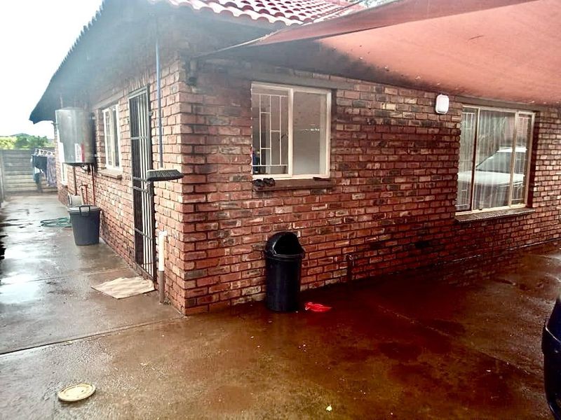 Exterior view of the rear brick facade featuring a covered patio area, security bars on windows, and an external geyser unit.