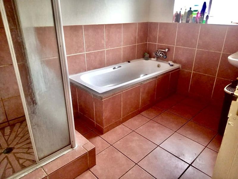 A dated bathroom featuring a built-in bathtub, a separate shower enclosure, and terracotta-style floor and wall tiling.