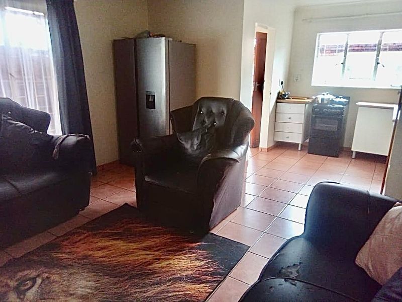 An open-plan living and kitchen area featuring tiled flooring, a functional kitchen layout with a freestanding stove, and direct access to adjacent rooms.