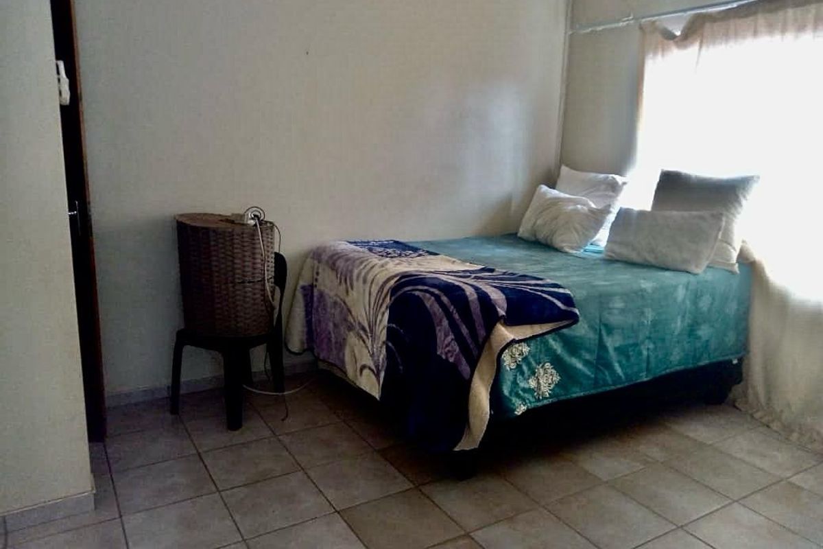 A functional bedroom featuring tiled flooring, a wall-mounted air conditioning unit, and a window with natural light.