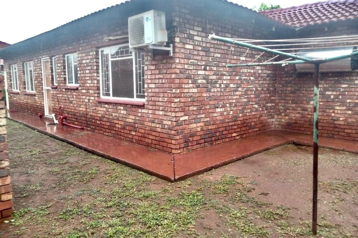 Rear exterior view of the house featuring face brick walls, tiled roof, security bars on windows, and an external air conditioning unit.