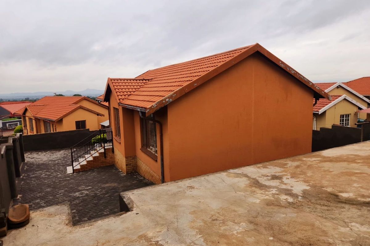 Rear view of a residential property featuring terracotta roof tiles, a paved driveway, and a concrete retaining wall with an external staircase.