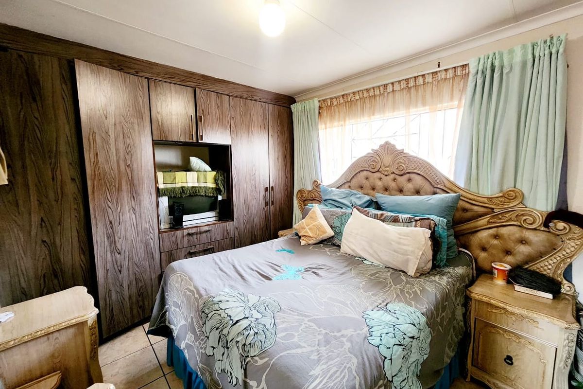 A bedroom featuring built-in wooden cupboards, tiled flooring, and security bars on the window.