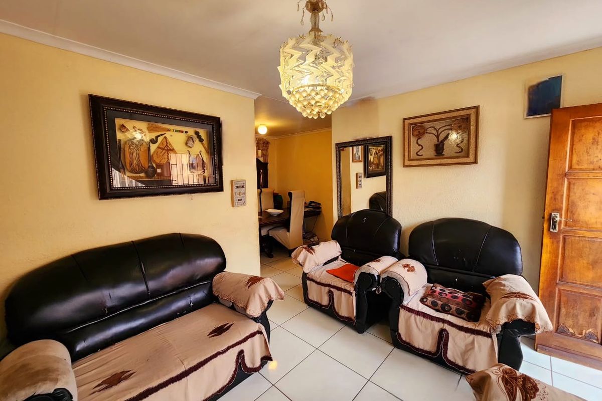 A living room featuring tiled flooring and a decorative crystal chandelier, with access to an adjacent dining area.