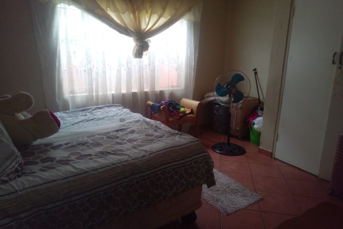 A bedroom featuring tiled flooring, a large window with natural light, and a built-in cupboard door.