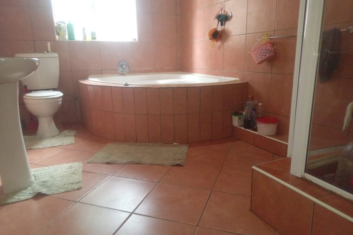 A dated bathroom featuring a corner bathtub, pedestal basin, and shower enclosure with terracotta-style floor and wall tiling.