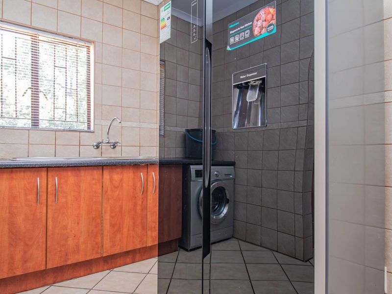 A functional laundry room featuring built-in wooden cabinetry, a stainless steel sink, tiled walls, and tiled flooring.