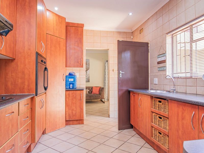 A functional kitchen featuring wood-finish cabinetry, built-in oven, extractor fan, and tiled splashbacks with a view into the adjacent living area.