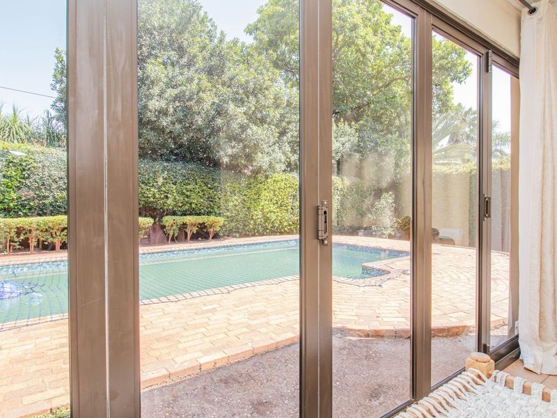 View from the interior through large sliding glass doors looking out onto a paved pool area and landscaped garden.