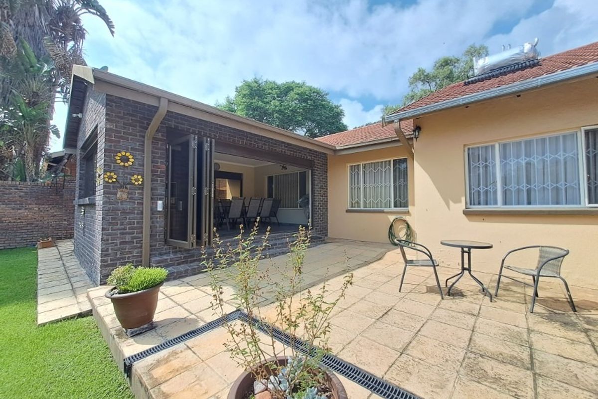 Rear exterior view featuring a paved patio area, brick-clad extension with folding doors, and a well-maintained garden lawn.