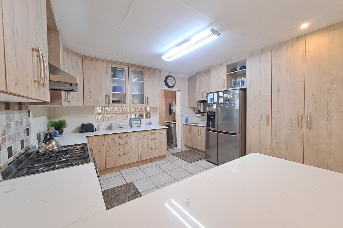 A well-appointed kitchen featuring light wood-grain cabinetry, stone countertops, a gas hob, extractor fan, and tiled flooring with a connected scullery area.