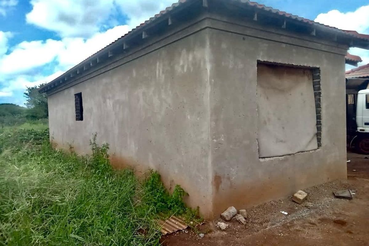 An unfinished exterior structure featuring raw cement walls, a tiled roof, and open window and door apertures awaiting final installation and finishing.