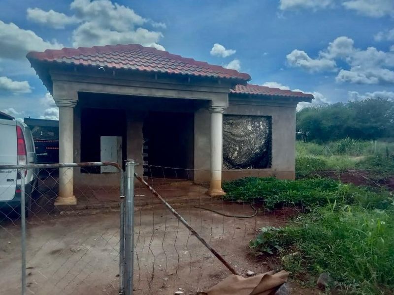A single-story house under construction featuring a tiled roof, decorative columns, and an unfinished facade with missing window installations.