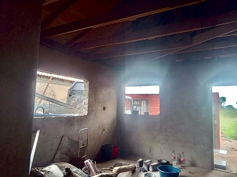 An unfinished interior space featuring exposed roof trusses, unplastered masonry walls, and open window apertures, offering a blank canvas for renovation.