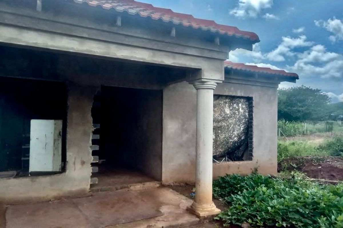 Exterior view of an unfinished house structure featuring a covered porch, concrete columns, and missing window and door installations.