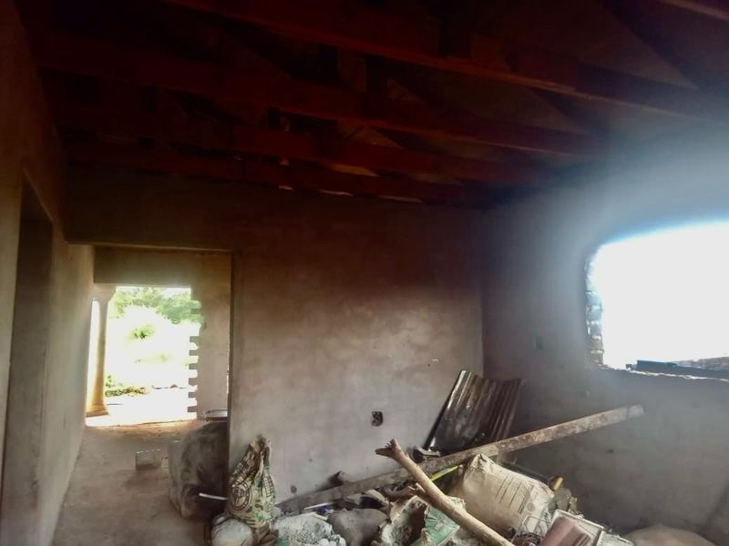 An unfinished interior room featuring exposed timber roof trusses and raw plastered walls, currently in a shell state requiring completion.