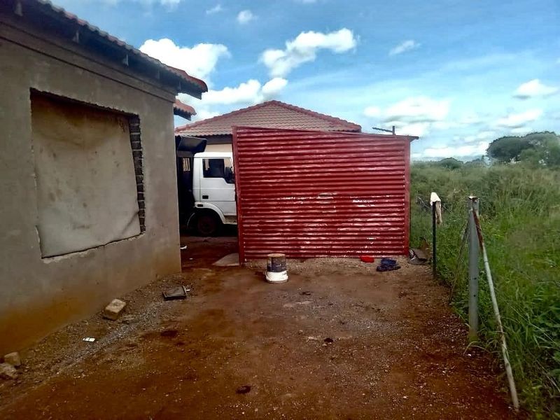 Exterior view of a property showing unfinished wall construction, corrugated metal fencing, and an unpaved yard area.