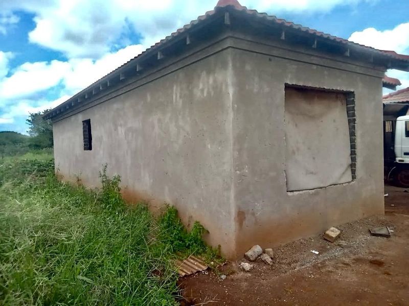 An unfinished exterior structure featuring raw cement walls, a tiled roof, and open window and door apertures awaiting final installation and finishing.