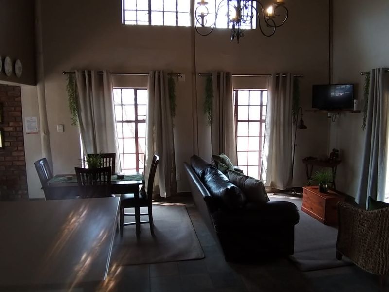 Spacious open-plan living and dining area featuring double volume ceilings, exposed brick accents, a wrought iron chandelier, and direct access to outdoor spaces.