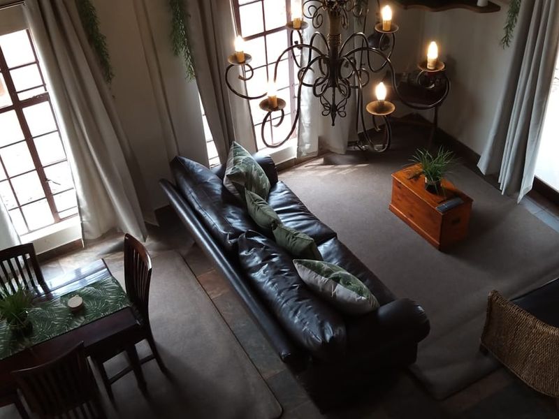 A spacious living area featuring high ceilings, a decorative wrought iron chandelier, large windows providing natural light, and tiled flooring.