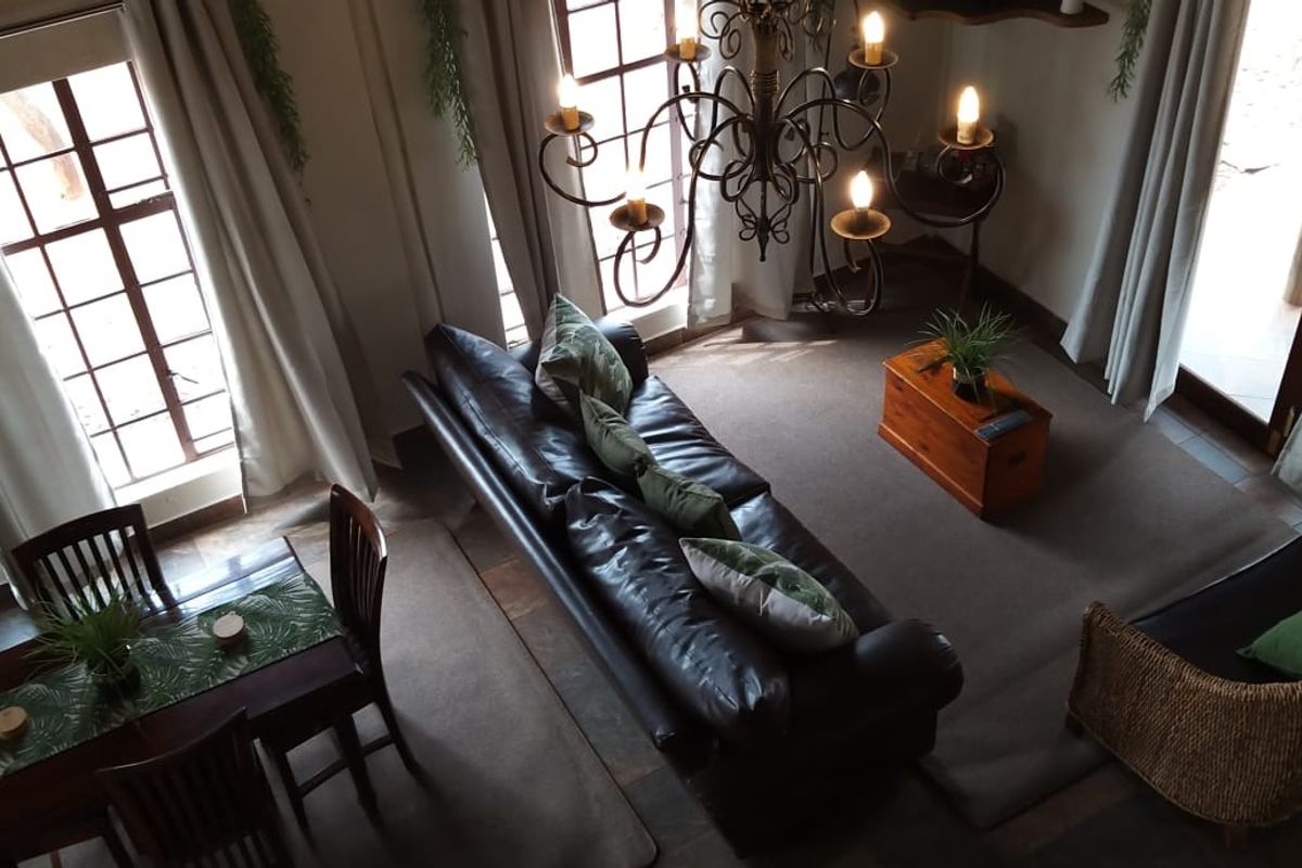 A spacious living area featuring high ceilings, a decorative wrought iron chandelier, large windows providing natural light, and tiled flooring.