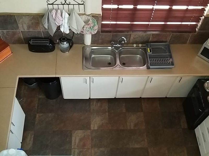 A functional U-shaped kitchen featuring laminate countertops, a double basin sink, built-in cabinetry, and an electric stove with tiled backsplash and flooring.
