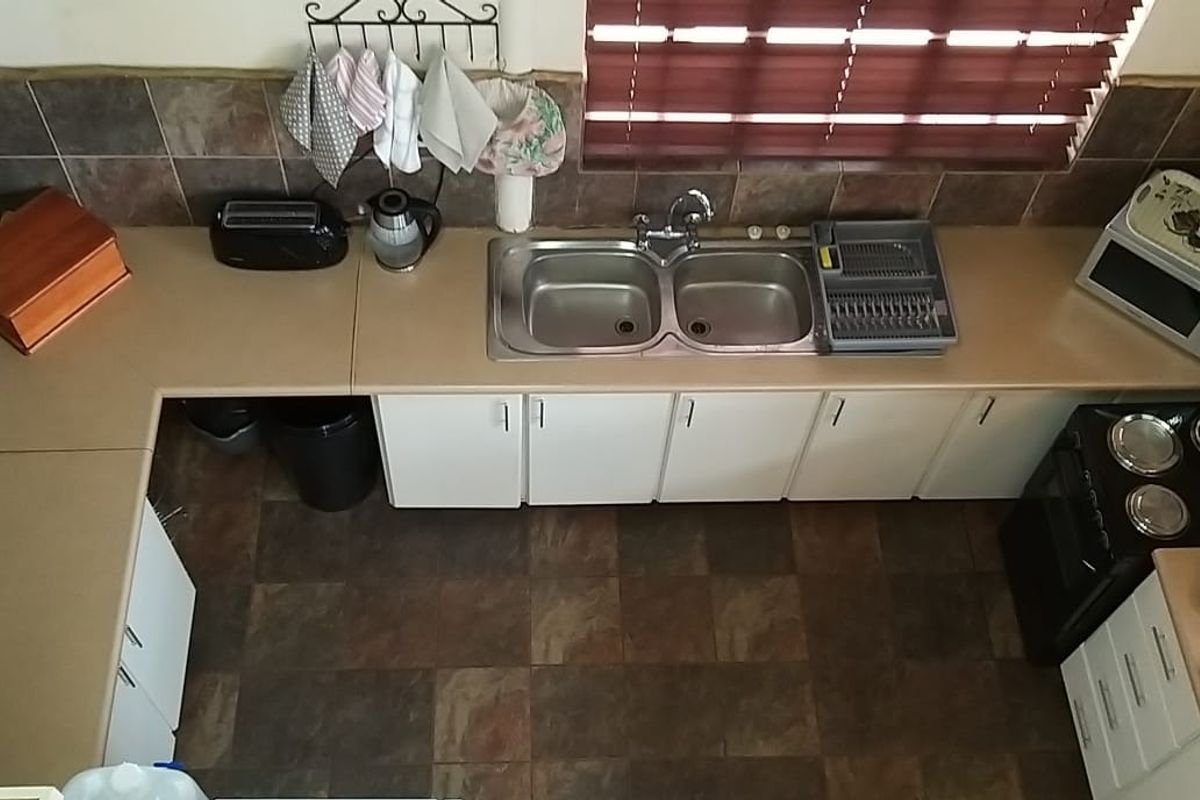 A functional U-shaped kitchen featuring laminate countertops, a double basin sink, built-in cabinetry, and an electric stove with tiled backsplash and flooring.