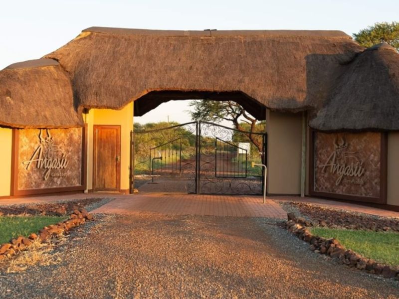 The main entrance gate of the farm property features a traditional thatched roof structure, stone-clad signage, and secure wrought iron gates.