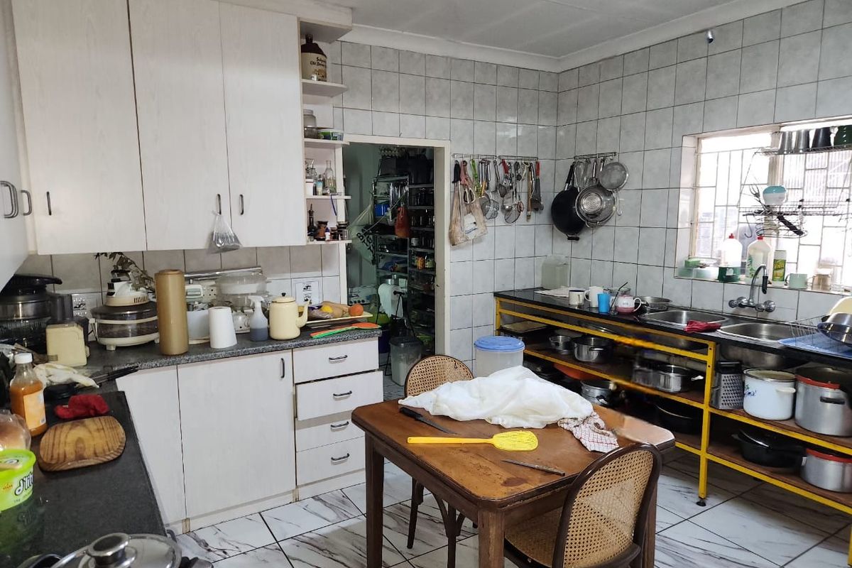 A functional kitchen featuring built-in cabinetry, tiled walls, and a double sink, with an adjacent scullery area.