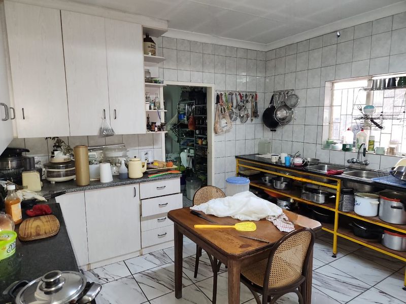 A functional kitchen featuring built-in cabinetry, tiled walls, and a double sink, with an adjacent scullery area.