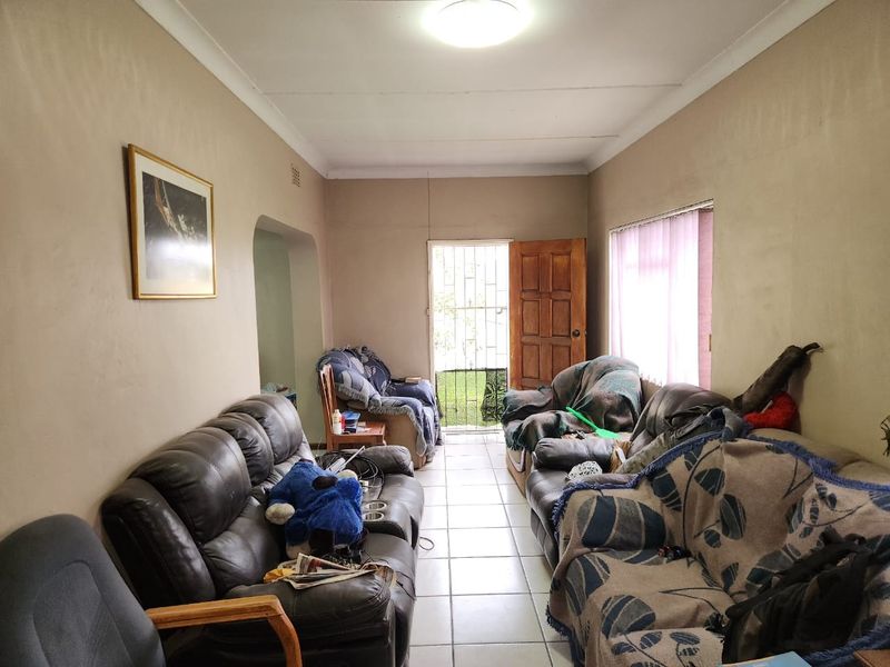 A living room featuring tiled flooring, a timber entrance door with a security gate, and standard ceiling lighting.
