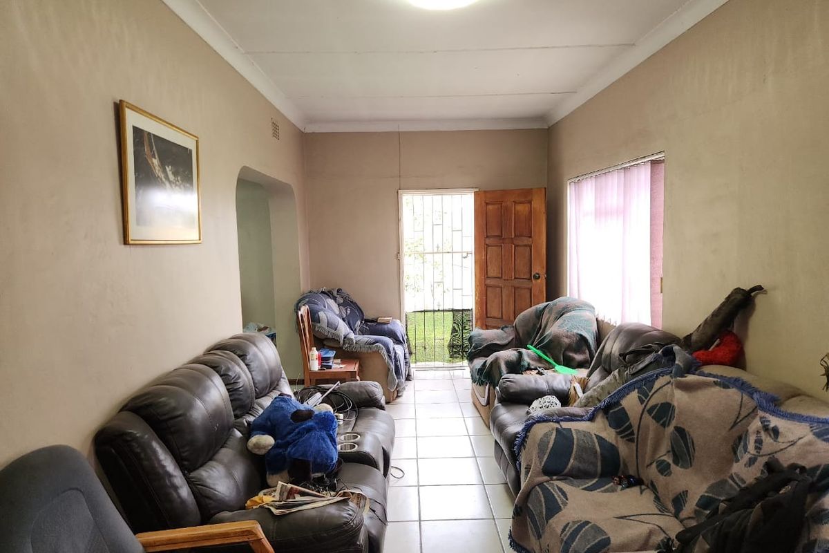 A living room featuring tiled flooring, a timber entrance door with a security gate, and standard ceiling lighting.