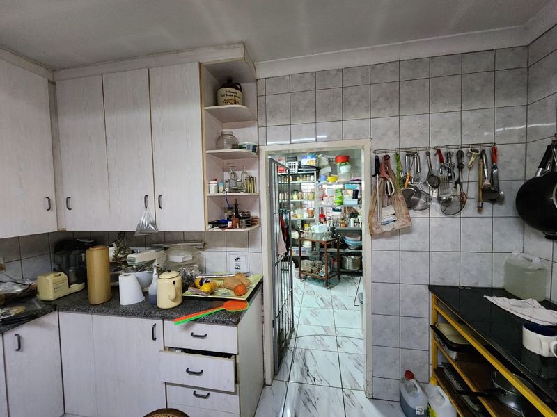 A functional kitchen featuring laminate cabinetry, granite countertops, and ceramic tiling, with an adjoining scullery area.